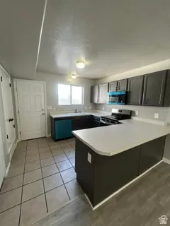 U-shaped kitchen featuring dark cabinetry, light countertops, a central island, and mixed flooring with tile and wood-finish planks