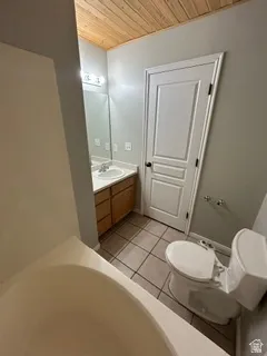 Light wood-paneled ceiling, wood-finish vanity with dual sinks, overhead vanity lighting, tiled flooring, and a built-in bathtub