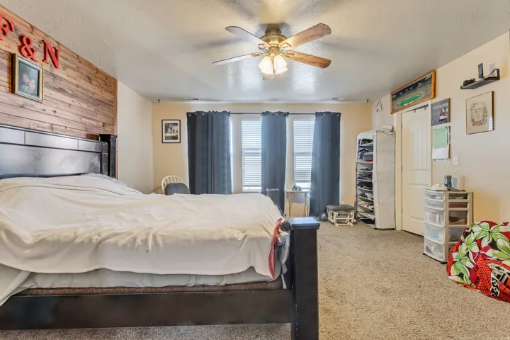 Spacious room featuring wood-plank accent wall, carpeted flooring, and a ceiling fan with integrated lighting