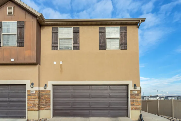 Stucco exterior with wood-paneled accents, two windows with decorative shutters, and an attached garage with a sectional door
