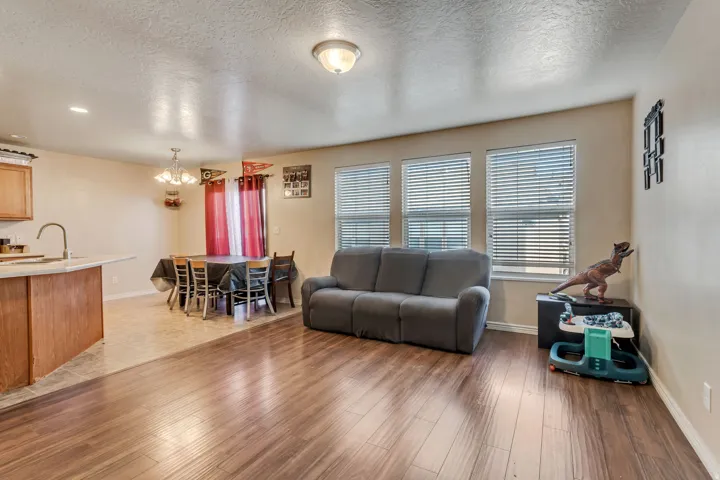 Wood-finish flooring throughout, multiple windows with blinds, a kitchen island with a built-in sink, and a dining area with a chandelier