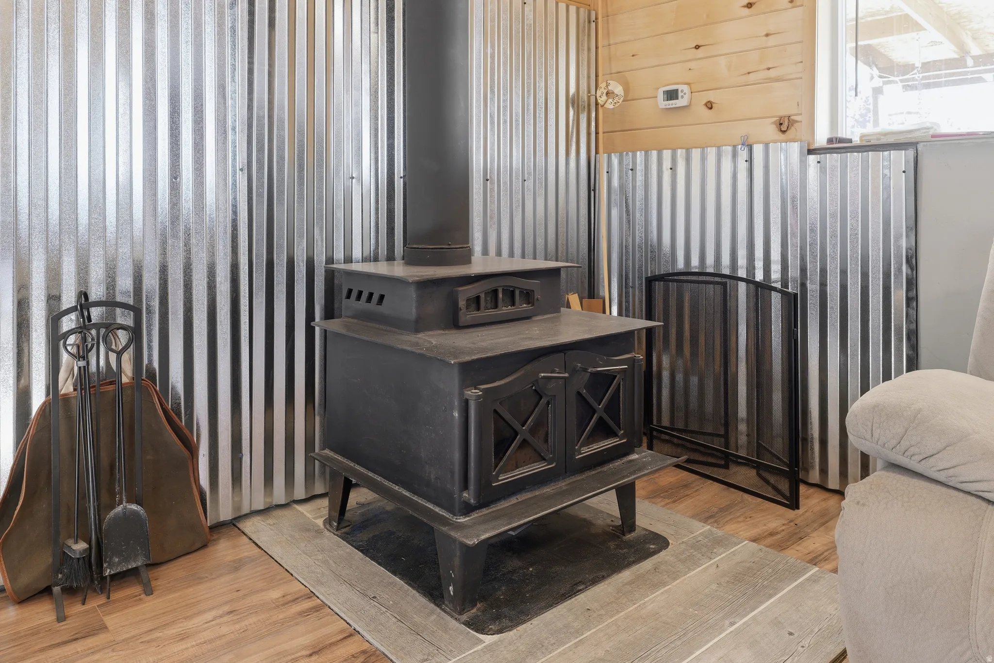 Cast iron wood-burning stove with a stovepipe, set against corrugated metal paneling and wood-finish flooring