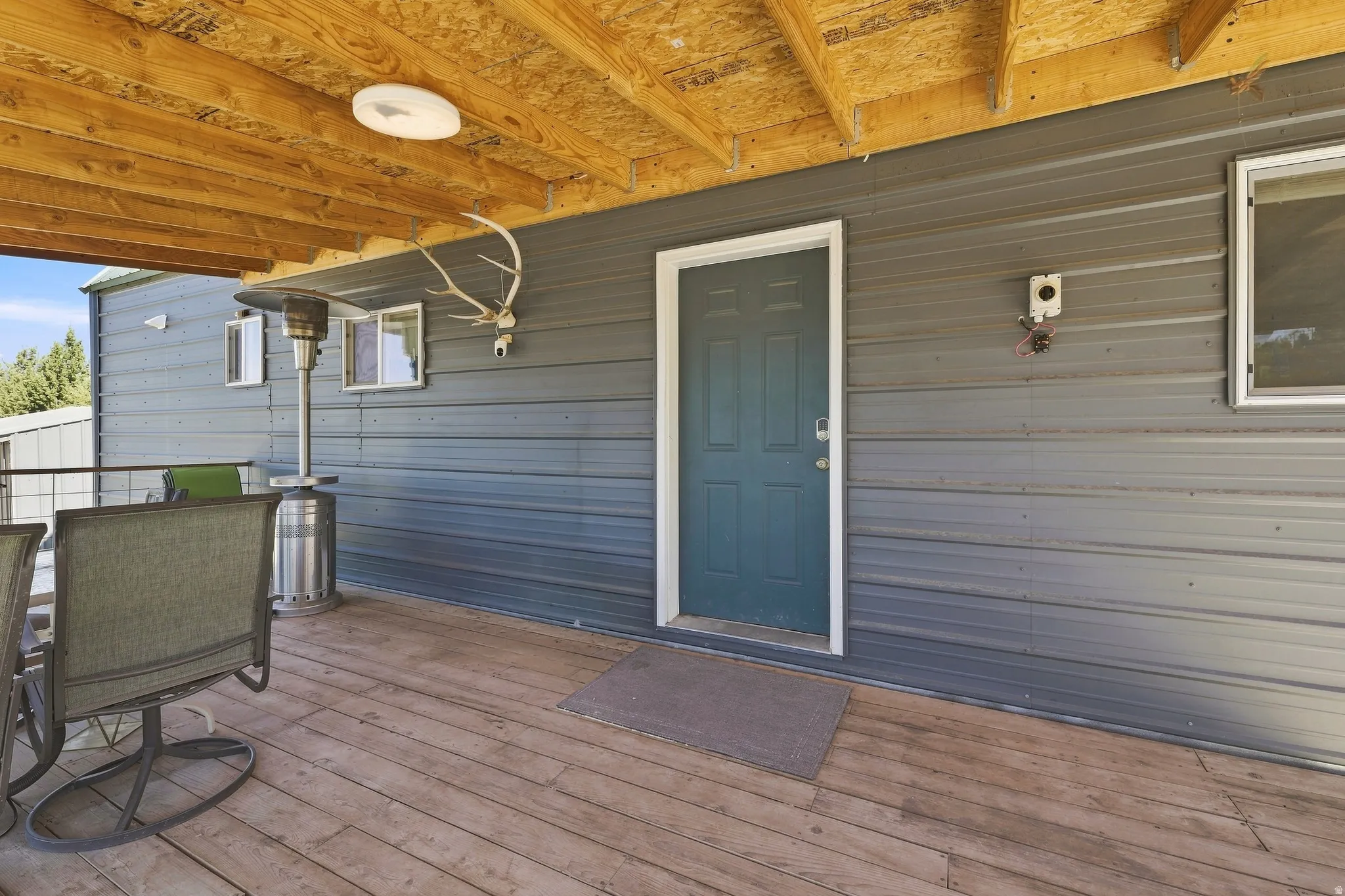 Expansive wood deck with exposed wood beam ceiling, metal siding exterior, and a paneled entry door