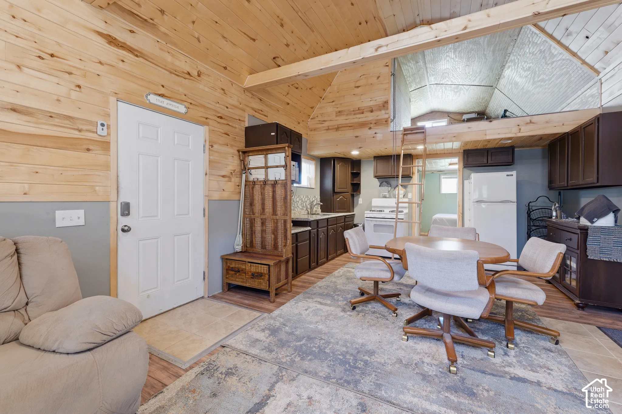 Wood-paneled ceilings with exposed beams, lofted area with ladder access, full kitchen with white appliances, wood-finish flooring, and built-in cabinetry