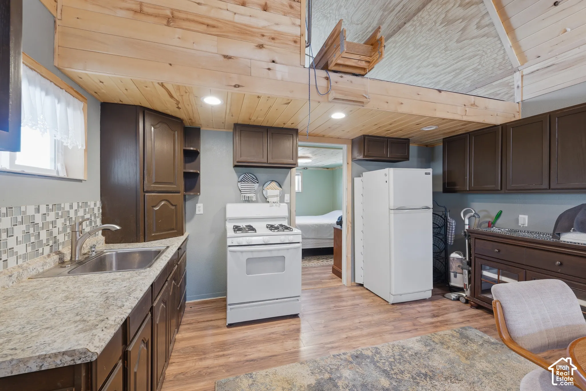 Kitchen featuring wood-finish flooring, dark wood-finish cabinetry, a stainless steel sink, and a tiled backsplash