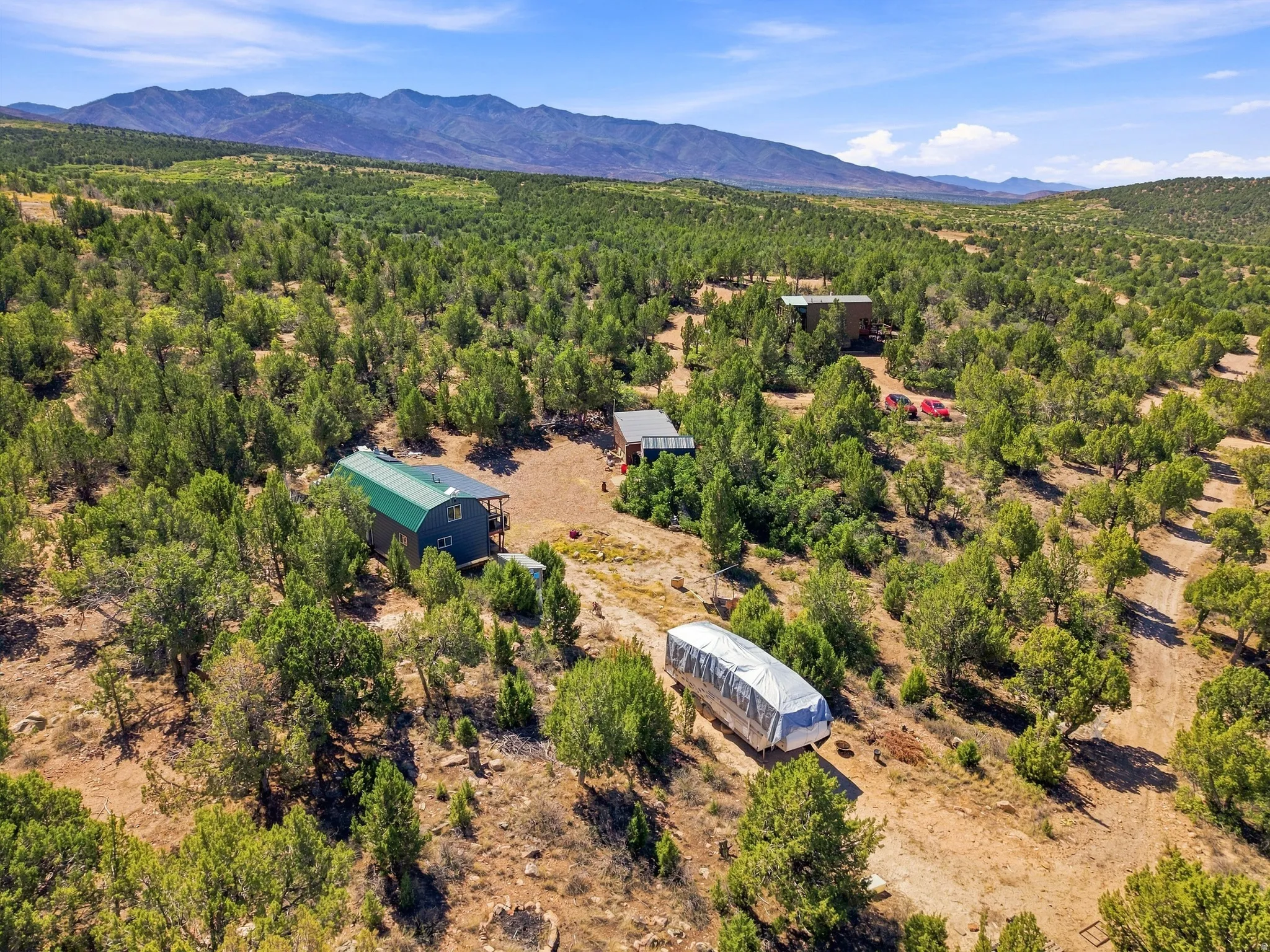 Multiple structures situated on a treed lot, with a prominent mountain range in the background
