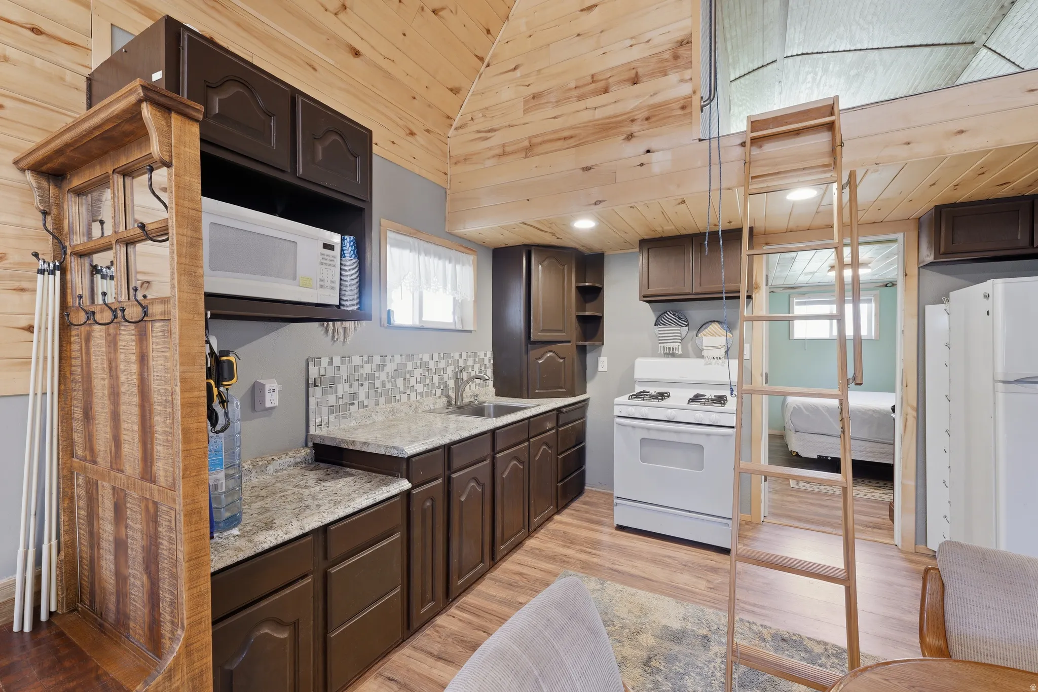 Compact kitchen featuring wood-finish flooring, dark wood cabinetry, granite-style countertops, and a mosaic tile backsplash