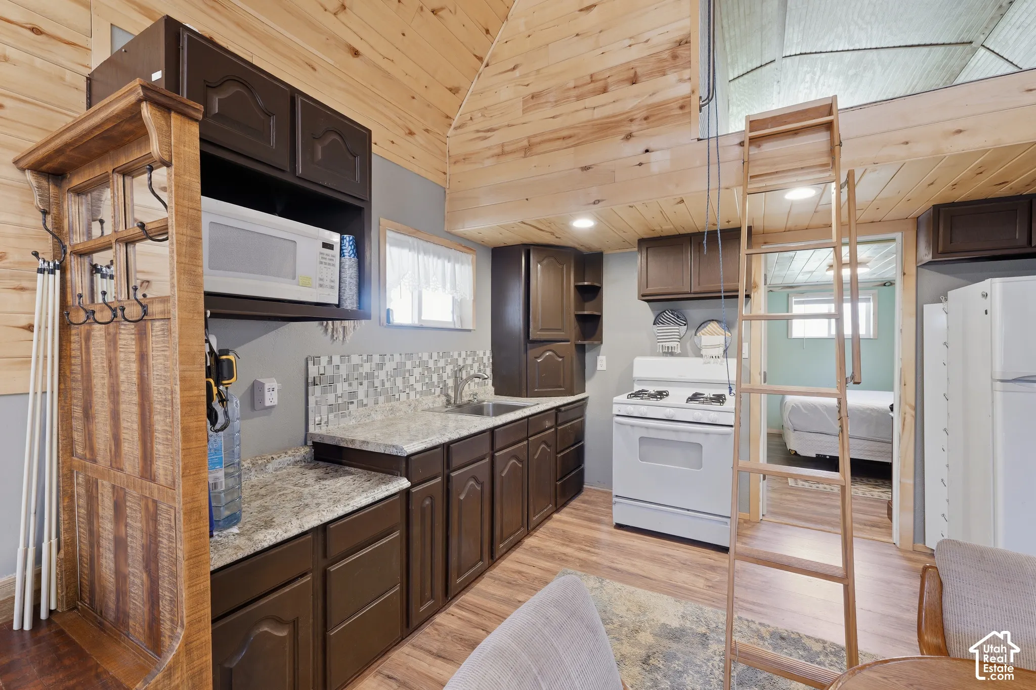 Compact kitchen featuring wood-finish flooring, dark wood cabinetry, granite-style countertops, and a mosaic tile backsplash