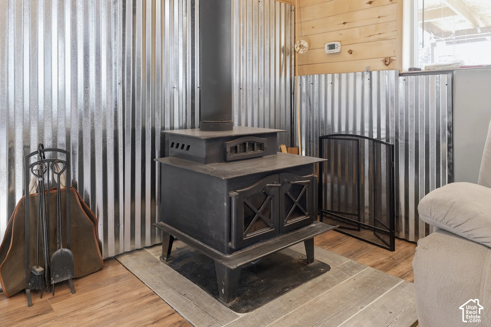 Cast iron wood-burning stove with a stovepipe, set against corrugated metal paneling and wood-finish flooring