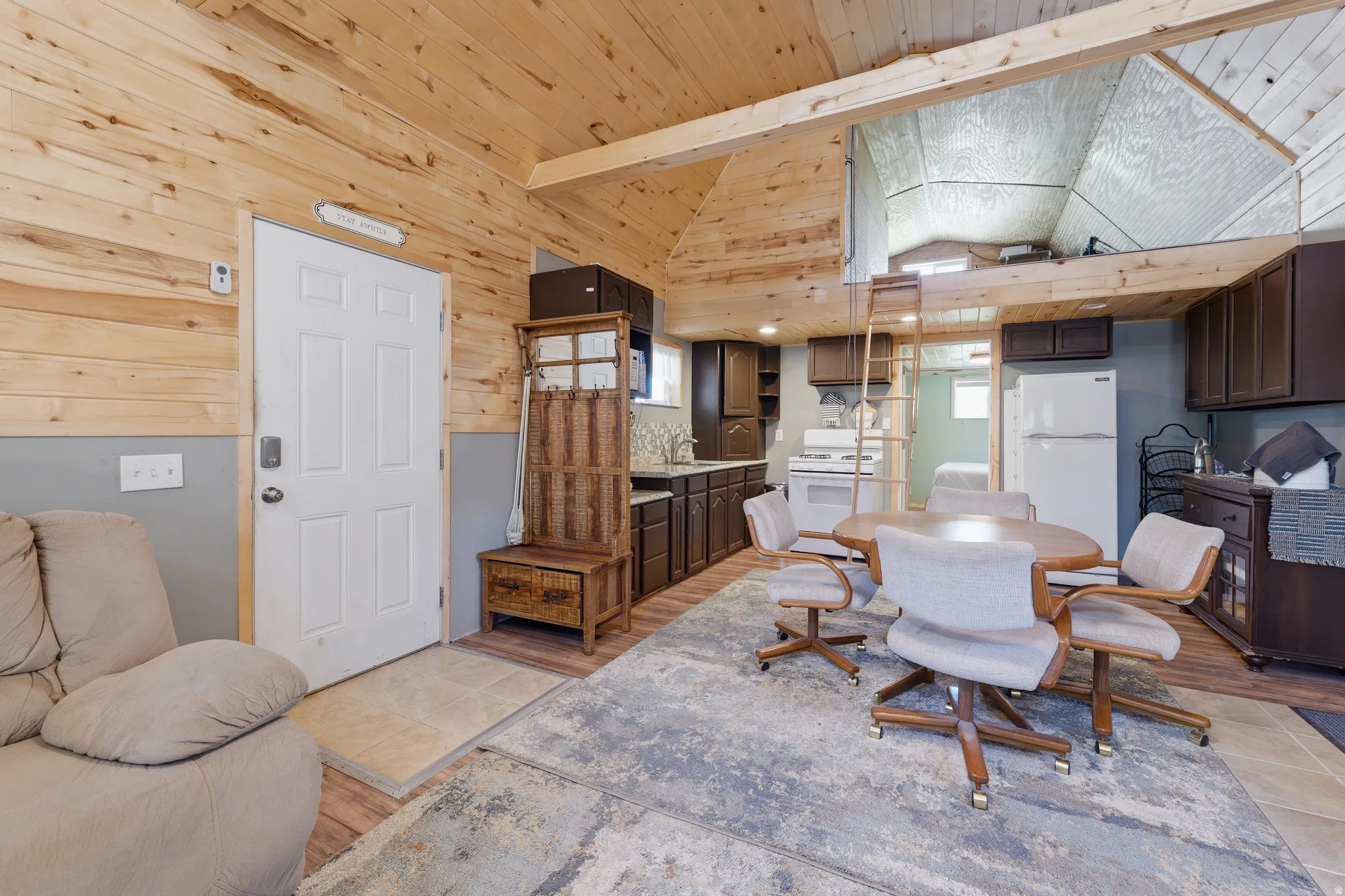 Wood-paneled ceilings with exposed beams, lofted area with ladder access, full kitchen with white appliances, wood-finish flooring, and built-in cabinetry