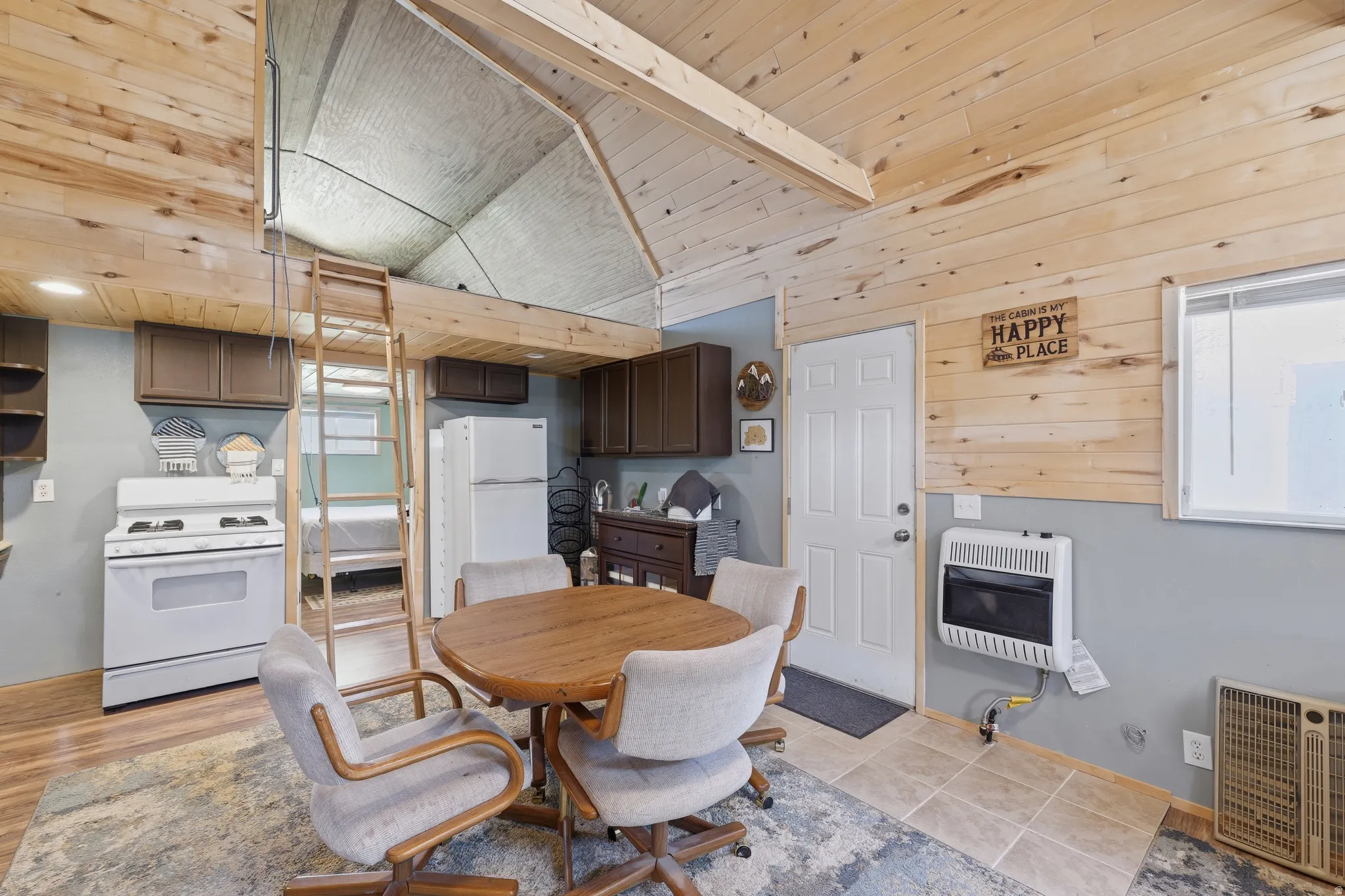 Wood-paneled walls and ceilings, wood-finish flooring, white appliances, built-in cabinetry, and a loft space with ladder access