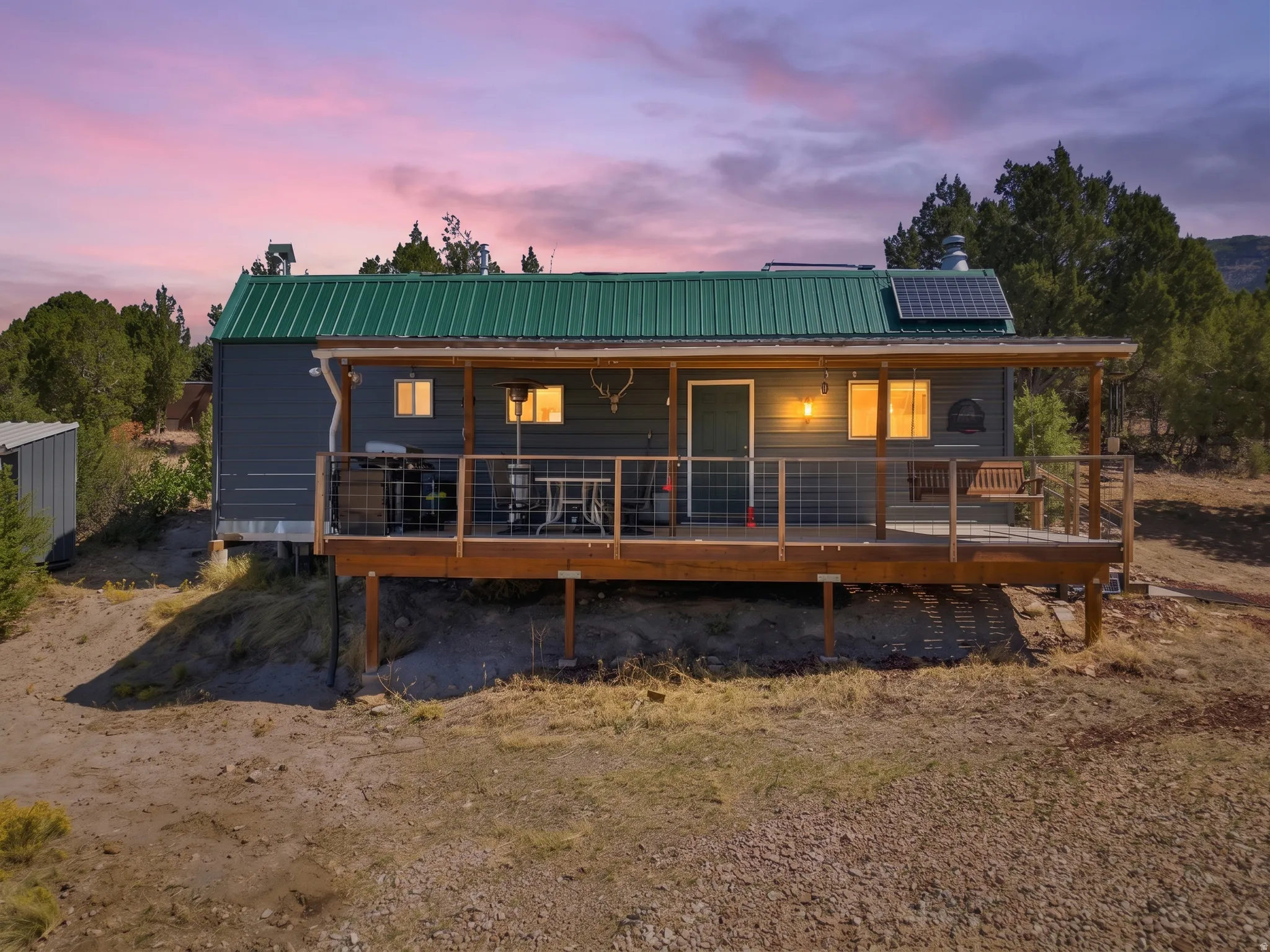 Exterior featuring a green metal roof, solar panels, and a wood-finish porch with a cable railing system