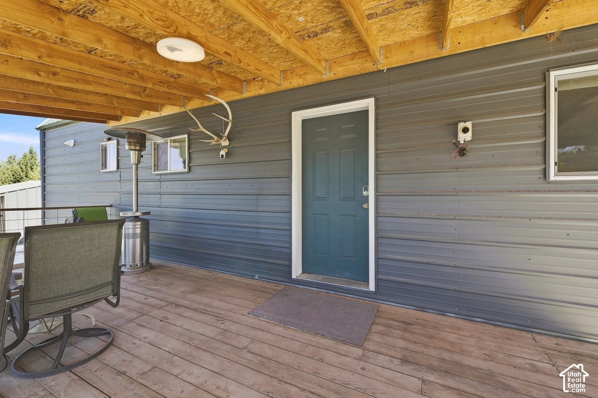 Expansive wood deck with exposed wood beam ceiling, metal siding exterior, and a paneled entry door