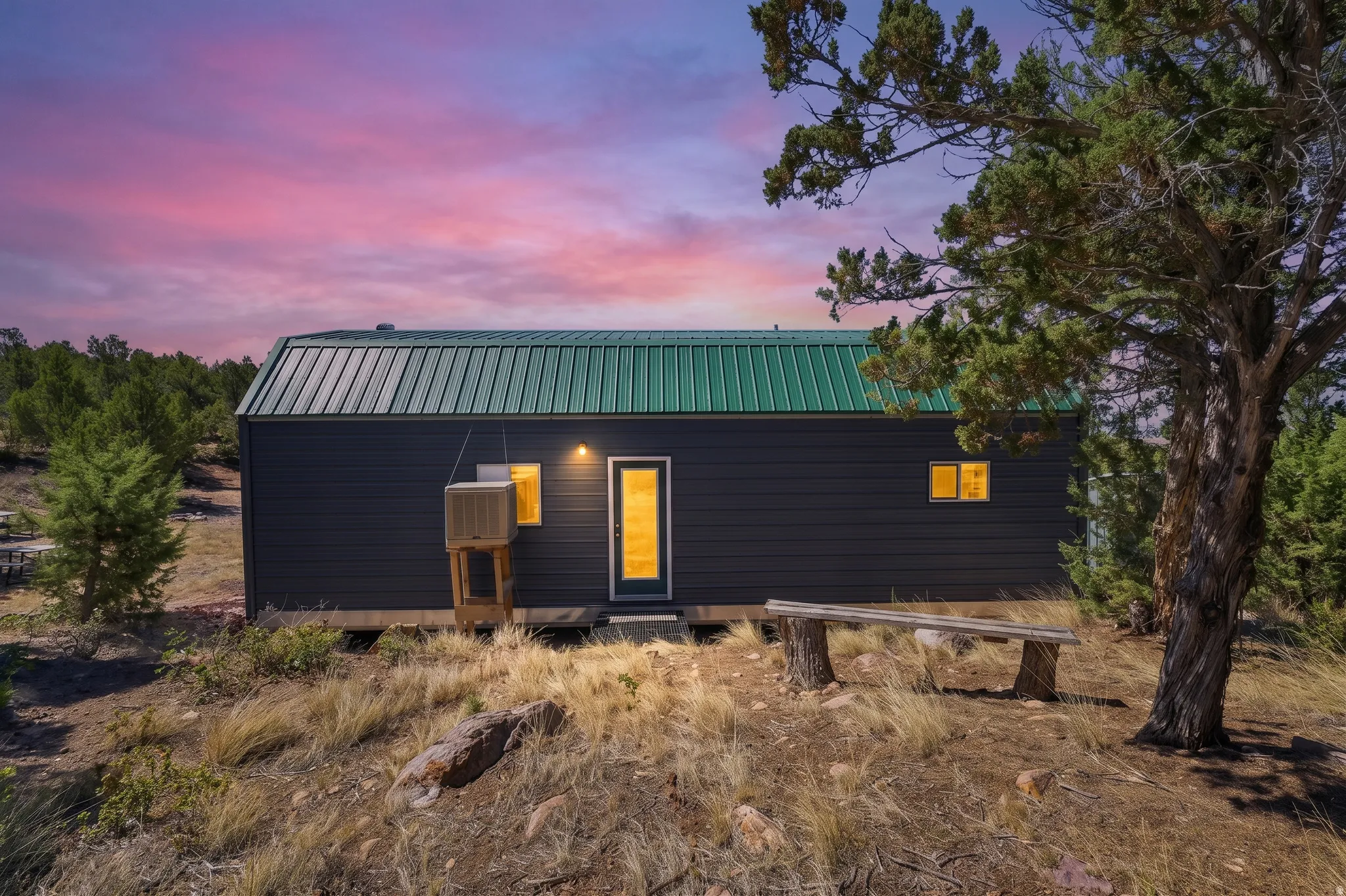Dark siding exterior with a green metal roof and an outdoor bench