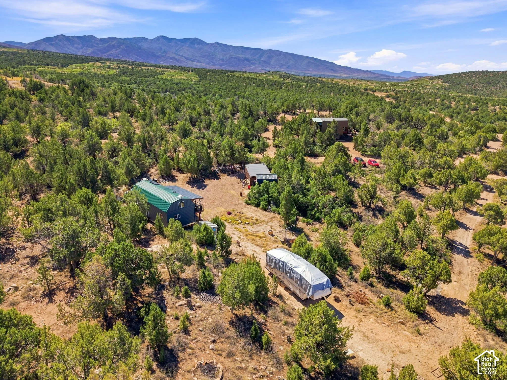 Multiple structures situated on a treed lot, with a prominent mountain range in the background