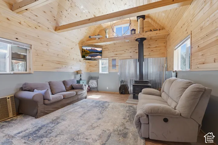 Vaulted wood plank ceiling, exposed structural beams, wood-finish flooring, and a wood-burning stove with corrugated metal backing
