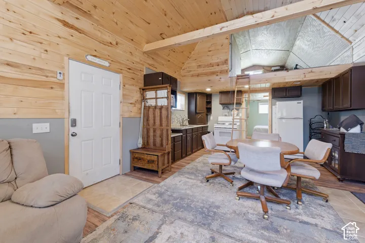 Wood-paneled ceilings with exposed beams, lofted area with ladder access, full kitchen with white appliances, wood-finish flooring, and built-in cabinetry