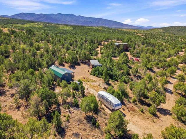 Multiple structures situated on a treed lot, with a prominent mountain range in the background