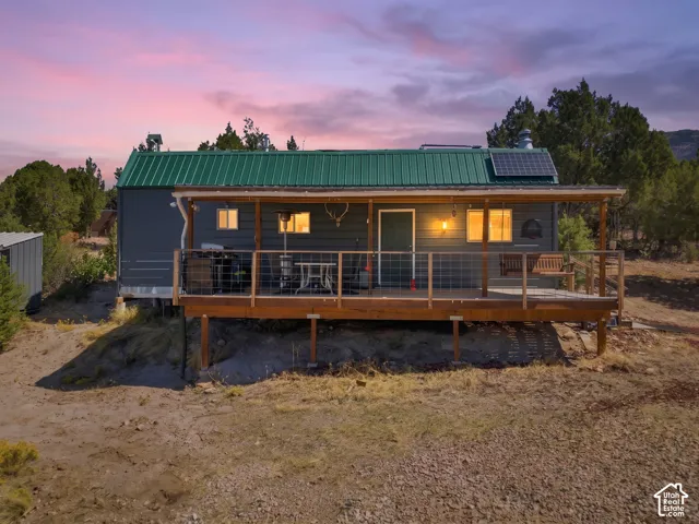 Exterior featuring a green metal roof, solar panels, and a wood-finish porch with a cable railing system