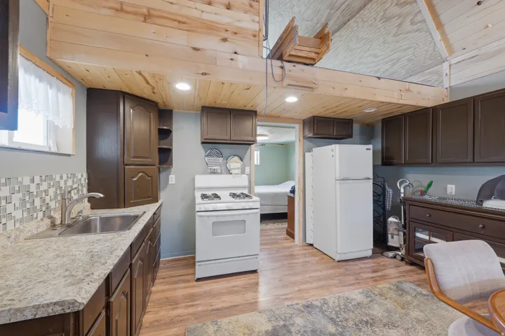 Kitchen featuring wood-finish flooring, dark wood-finish cabinetry, a stainless steel sink, and a tiled backsplash