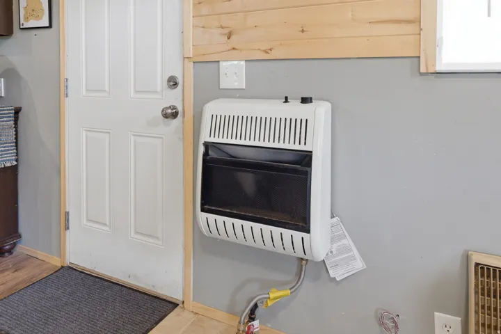 Wall-mounted heating unit with a white finish, positioned beneath a light wood-paneled wall and a window