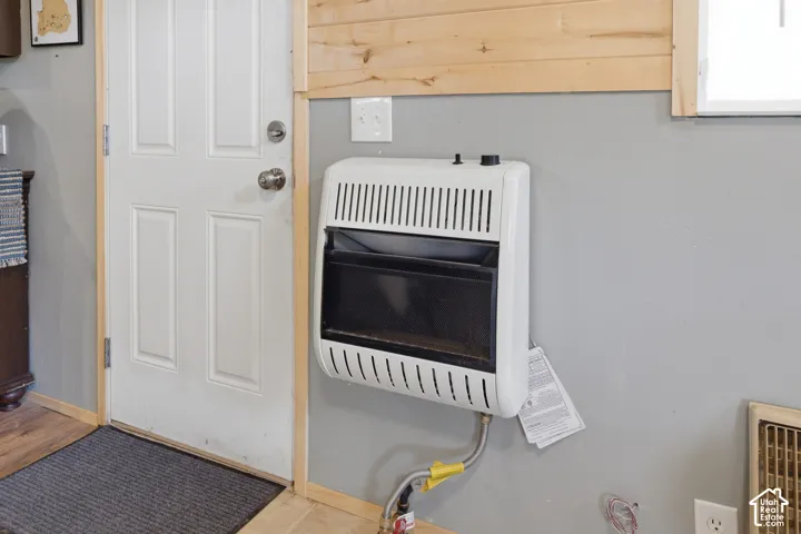 Wall-mounted heating unit with a white finish, positioned beneath a light wood-paneled wall and a window