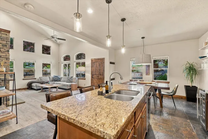 Kitchen island with granite countertop and dual under-mount sinks, wood-finish cabinetry, and pendant lighting