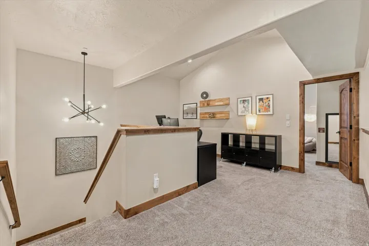 Loft area with vaulted ceiling, carpeted flooring, and a contemporary chandelier