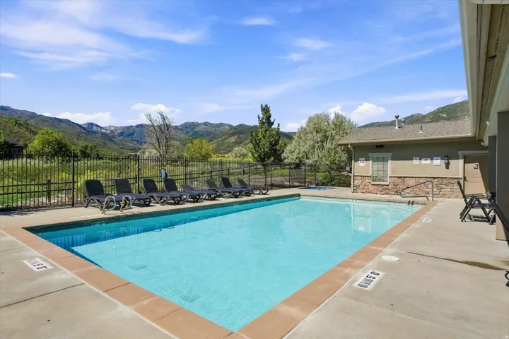 Outdoor swimming pool with concrete decking, a metal perimeter fence, and stone-clad building facade