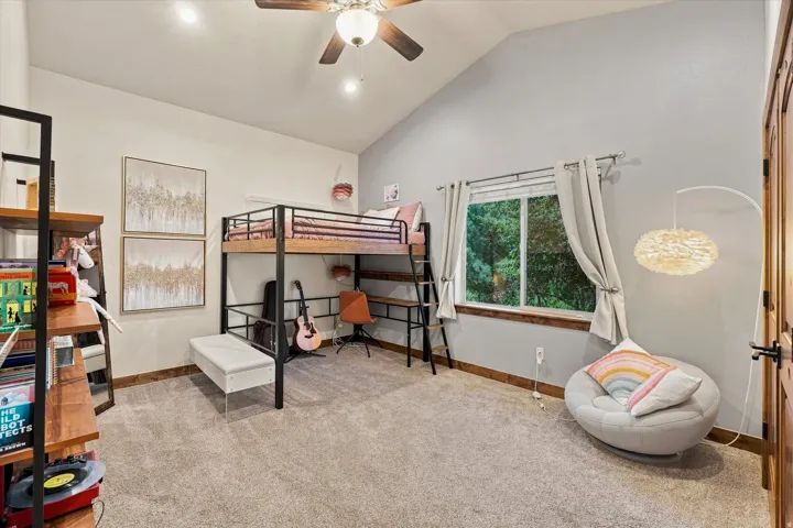 Carpeted room featuring a vaulted ceiling, ceiling fan, and a window with wood trim