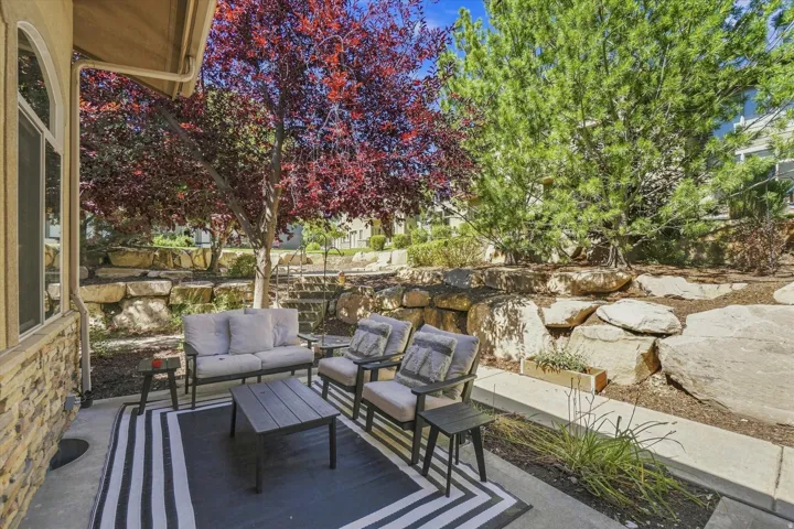 Concrete patio with a stone veneer exterior, framed by mature trees, and a terraced rock landscape