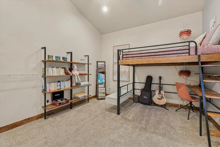 Integrated loft bed with a built-in desk, vaulted ceiling, and carpeted flooring