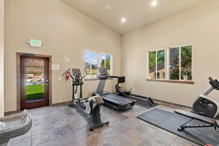 Vaulted ceiling exercise room with large windows, recessed lighting, and stone tile flooring
