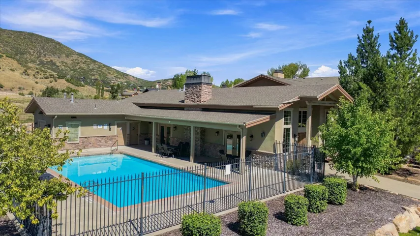Outdoor swimming pool with surrounding fencing, covered patio, stone-clad chimney, and mountain backdrop