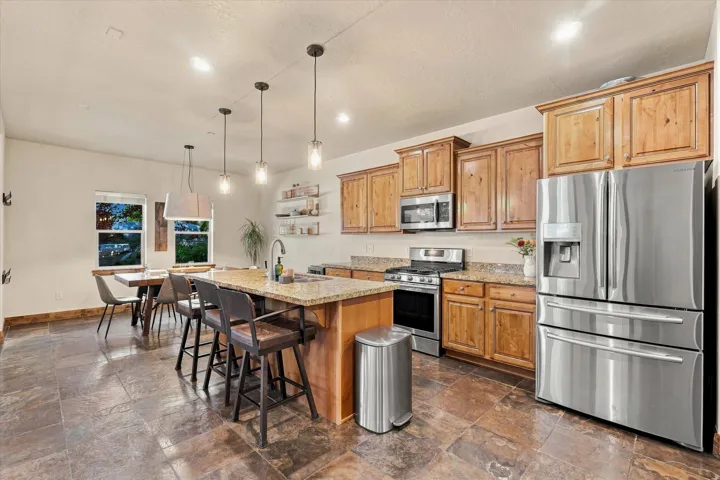 Kitchen featuring an island with stone countertop, stainless steel appliances, wood cabinetry, and large format tile flooring