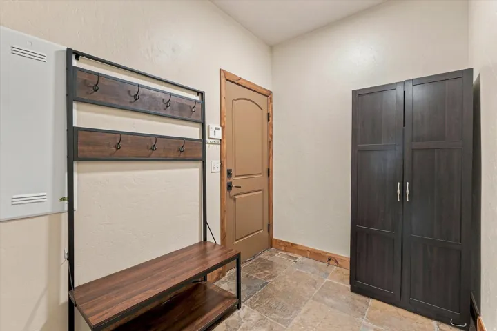 Tiled flooring, paneled interior door with wood trim, wood-finish storage cabinet, and wood-finish hall tree with metal hooks and a bench