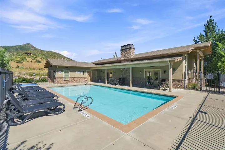 Outdoor swimming pool with concrete decking, a stone-clad building, and a mountain backdrop