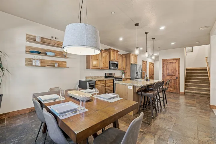 Open-concept kitchen and dining area featuring wood cabinetry, stainless steel appliances, a center island with bar seating, and stone-look tile flooring