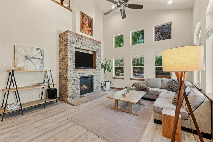 High ceilings, stone-clad fireplace with hearth, recessed lighting, wood-finish flooring, and multiple windows