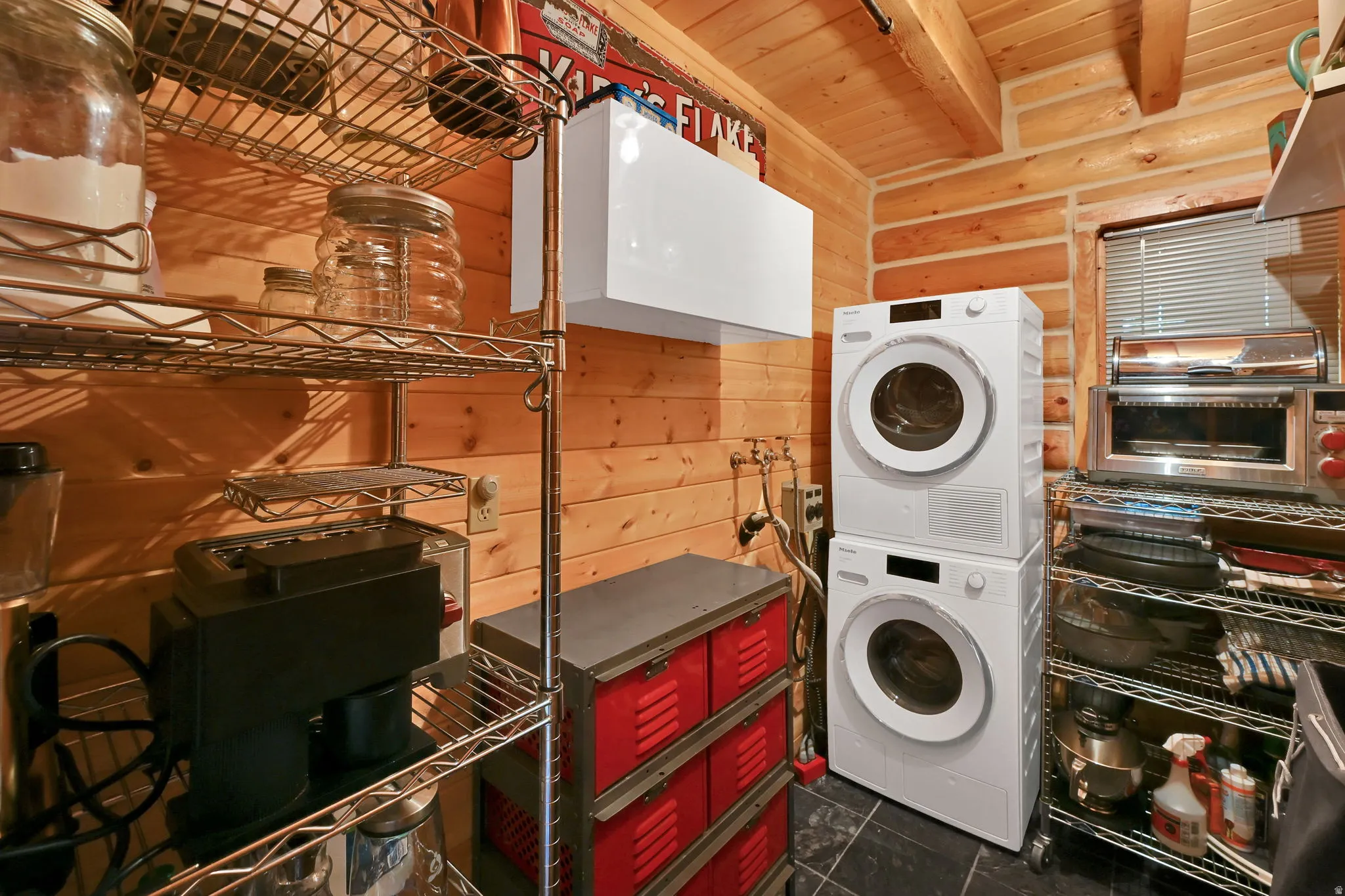 Wood-paneled walls featuring a stacked washer and dryer, stainless steel shelving, and a dark tile floor