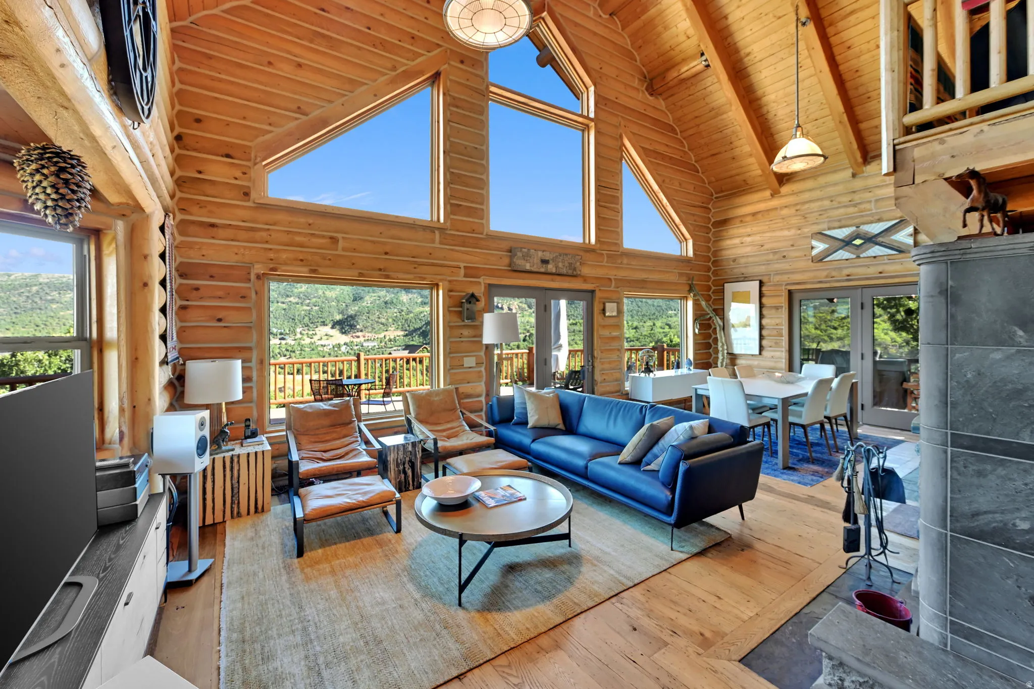 Vaulted wood plank ceilings with exposed beams, large picture windows, wood-finish flooring, and a stone-clad fireplace