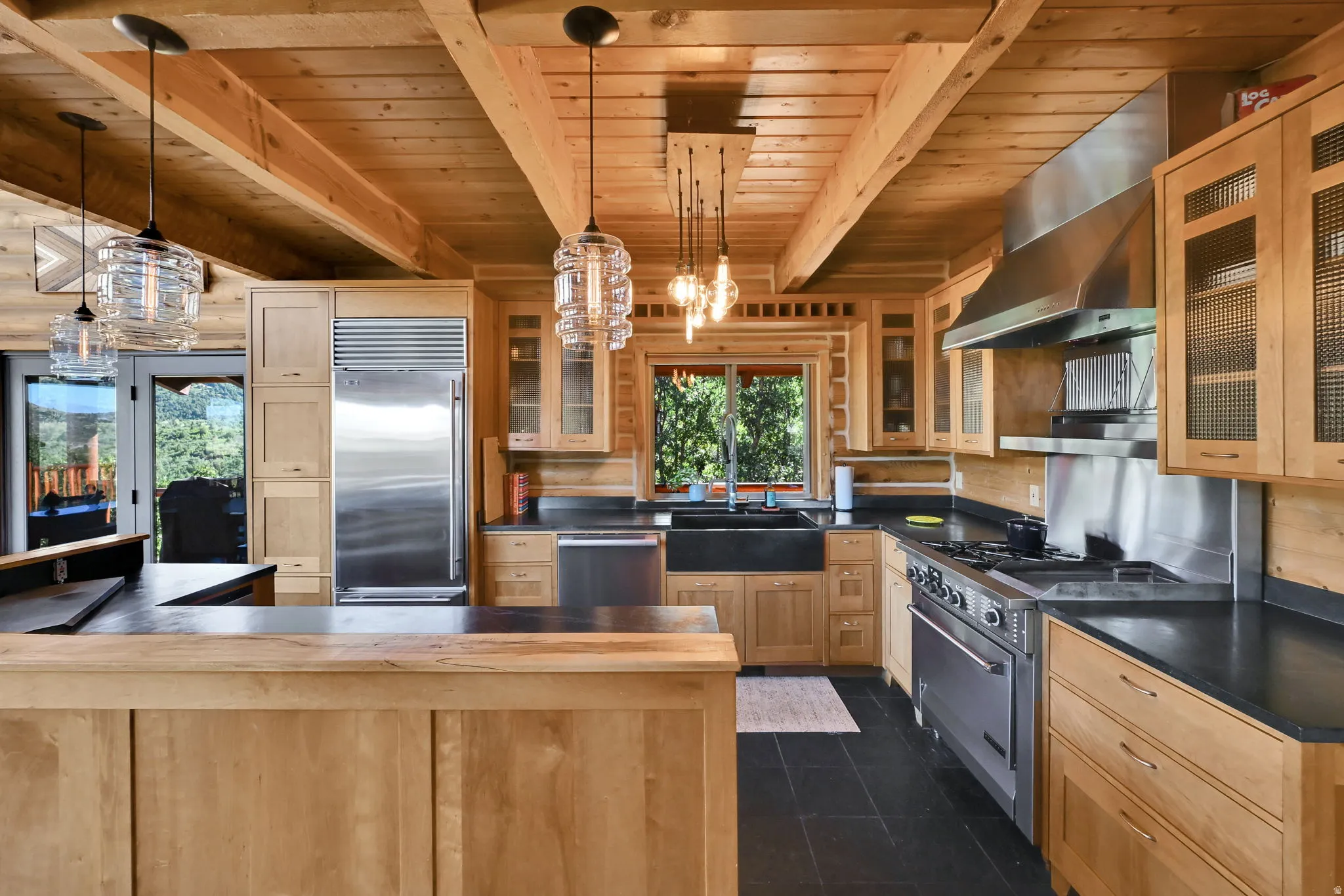 Kitchen featuring wood beam ceiling, wood-finish cabinetry, stainless steel appliances, dark countertops, and dark floor tiling