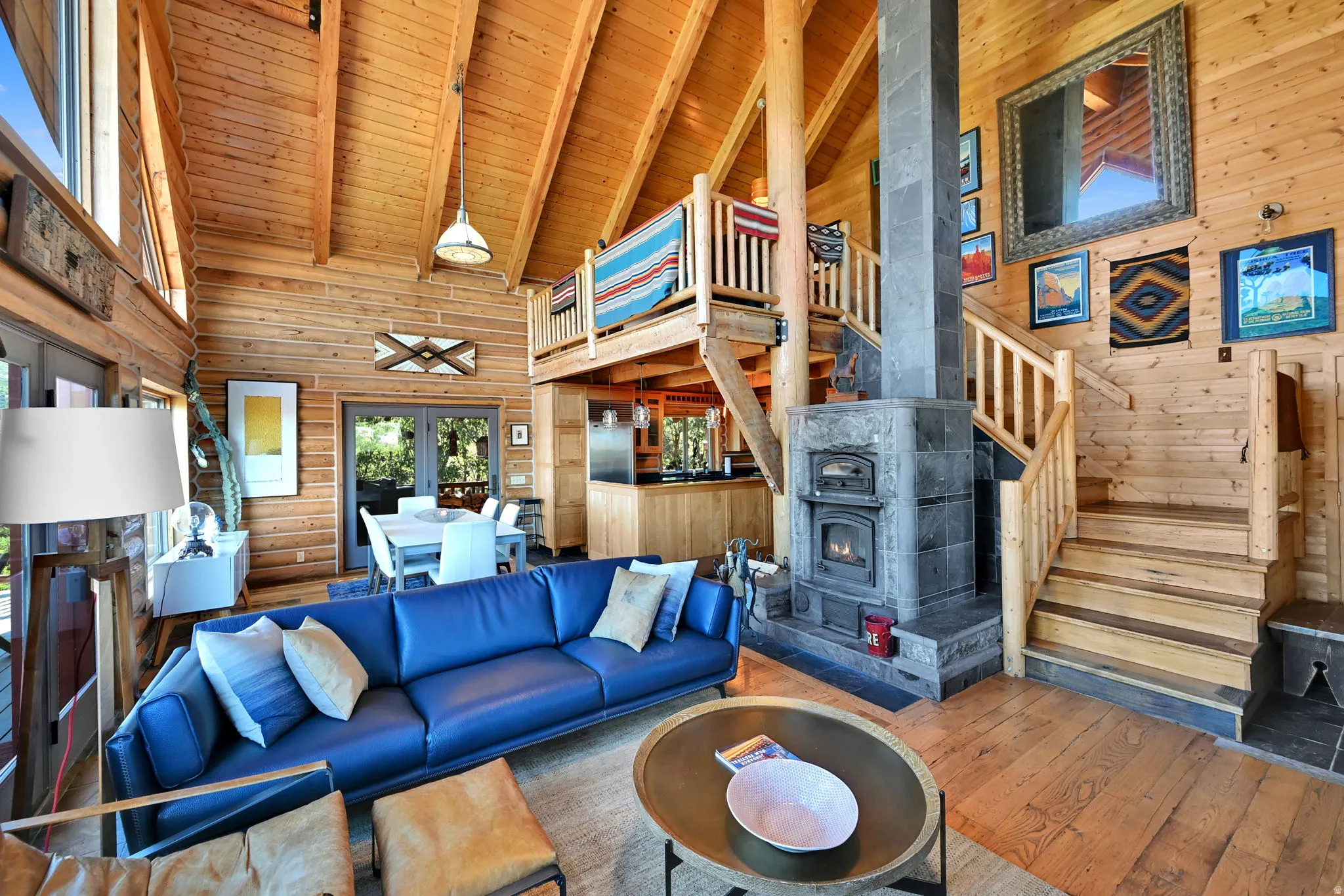 Vaulted wood-paneled ceilings, stone-clad fireplace with wood stove, exposed wood beams, wood-finish flooring, and a wooden staircase