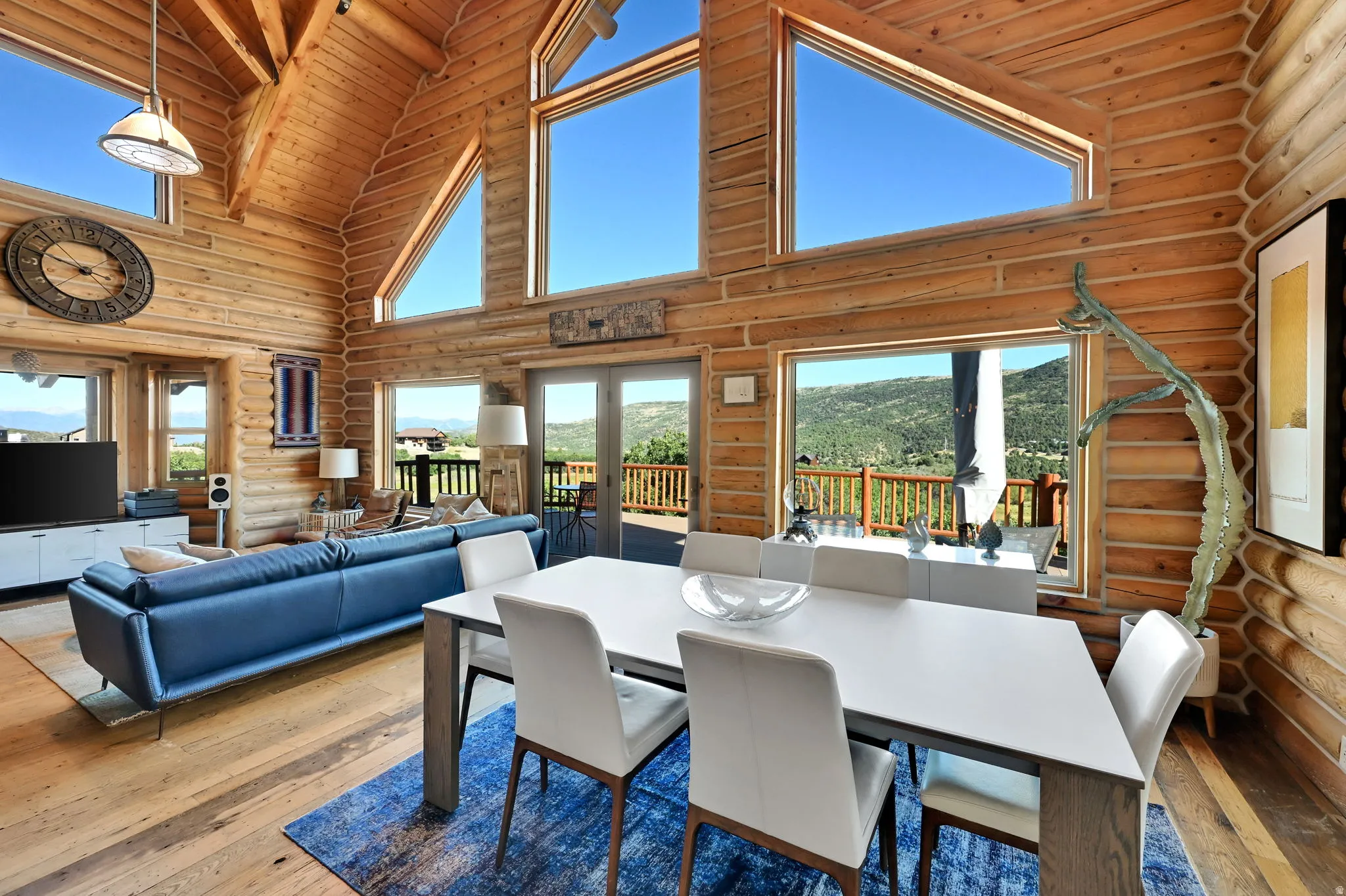 Vaulted wood-paneled ceilings, wood-finish flooring, exposed log walls, multi-pane windows, and glass doors opening to an outdoor deck