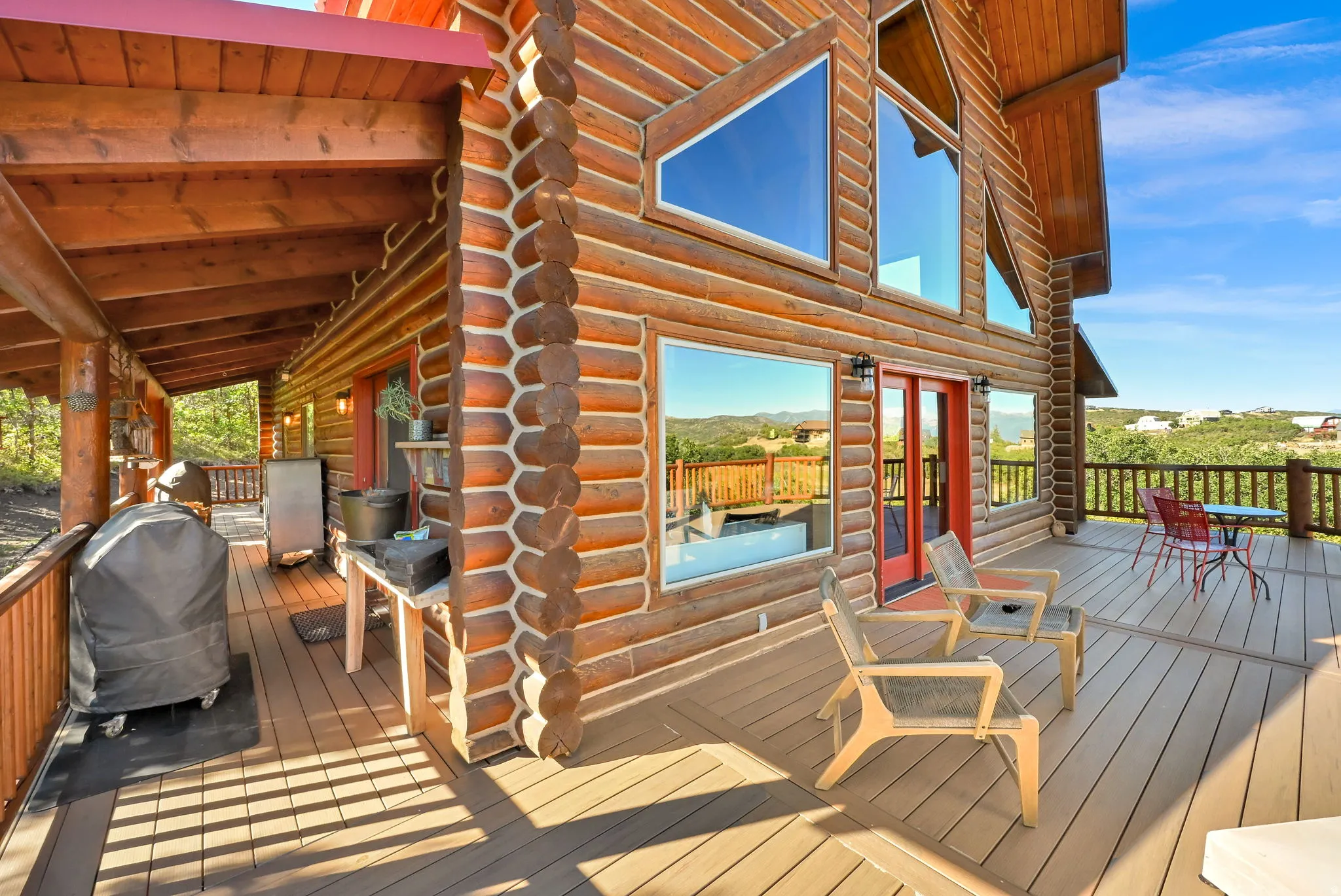 Log home exterior with a multi-level deck, expansive windows, and a covered patio area