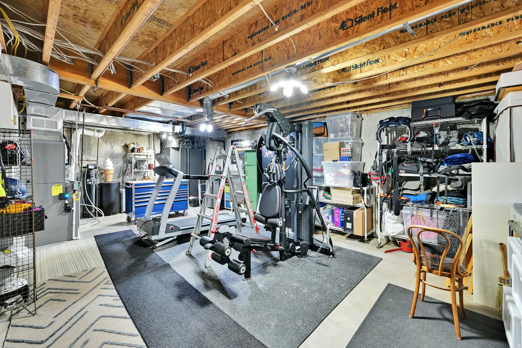Unfinished basement featuring exposed wood joists, concrete walls, ductwork, and overhead lighting