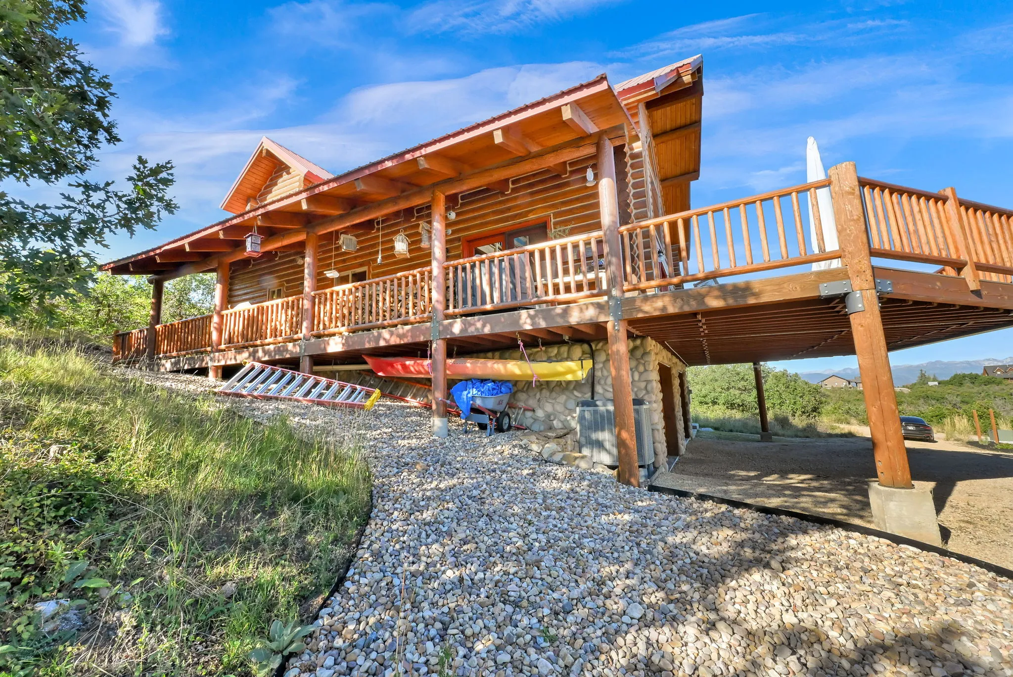 Wood-sided exterior featuring an elevated deck with wood railings, a gravel path, a stone foundation, and natural landscaping