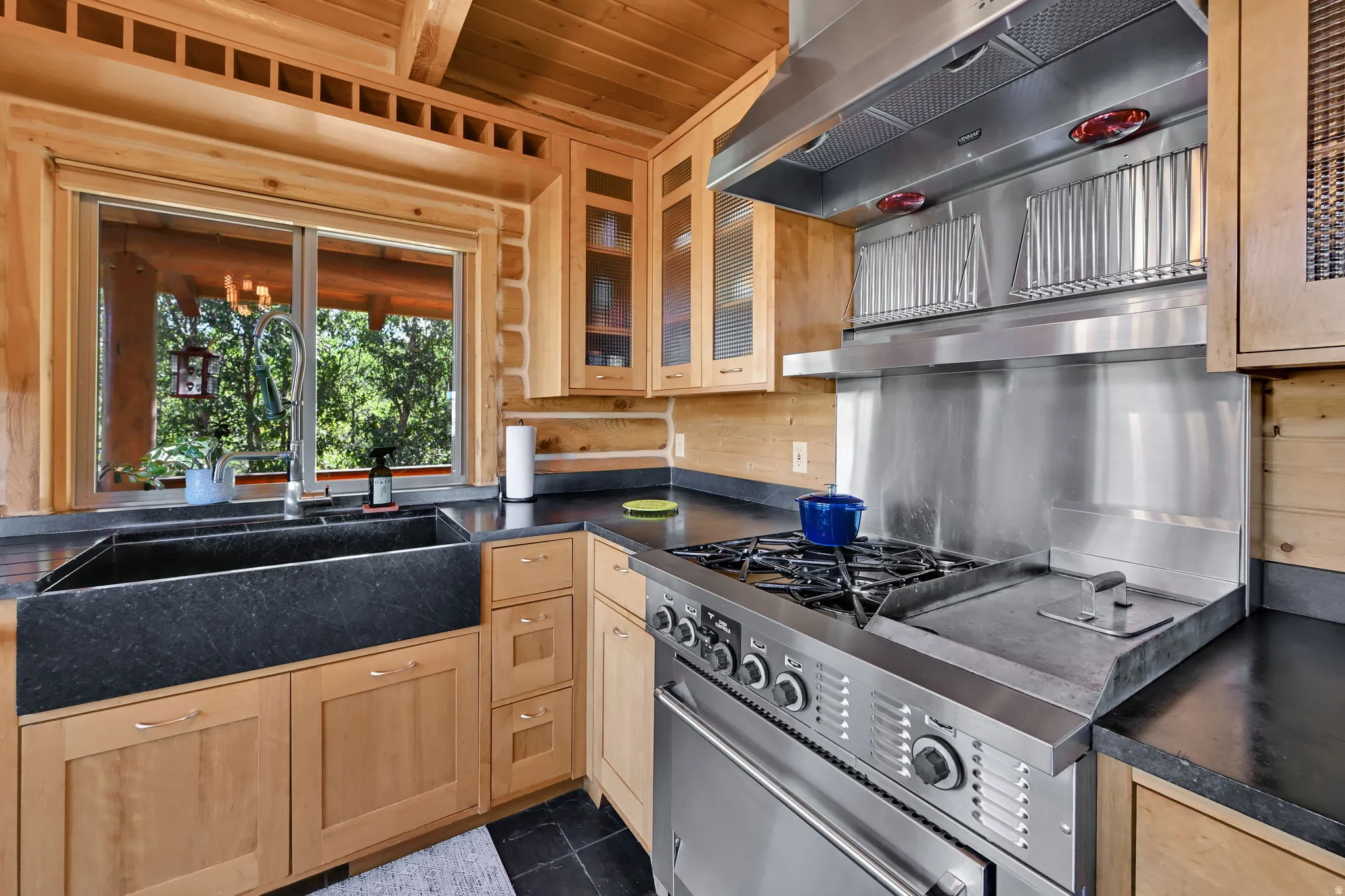 Wood plank walls and ceiling, stainless steel professional-grade range with griddle, stainless steel range hood, black farmhouse sink, and light wood cabinetry