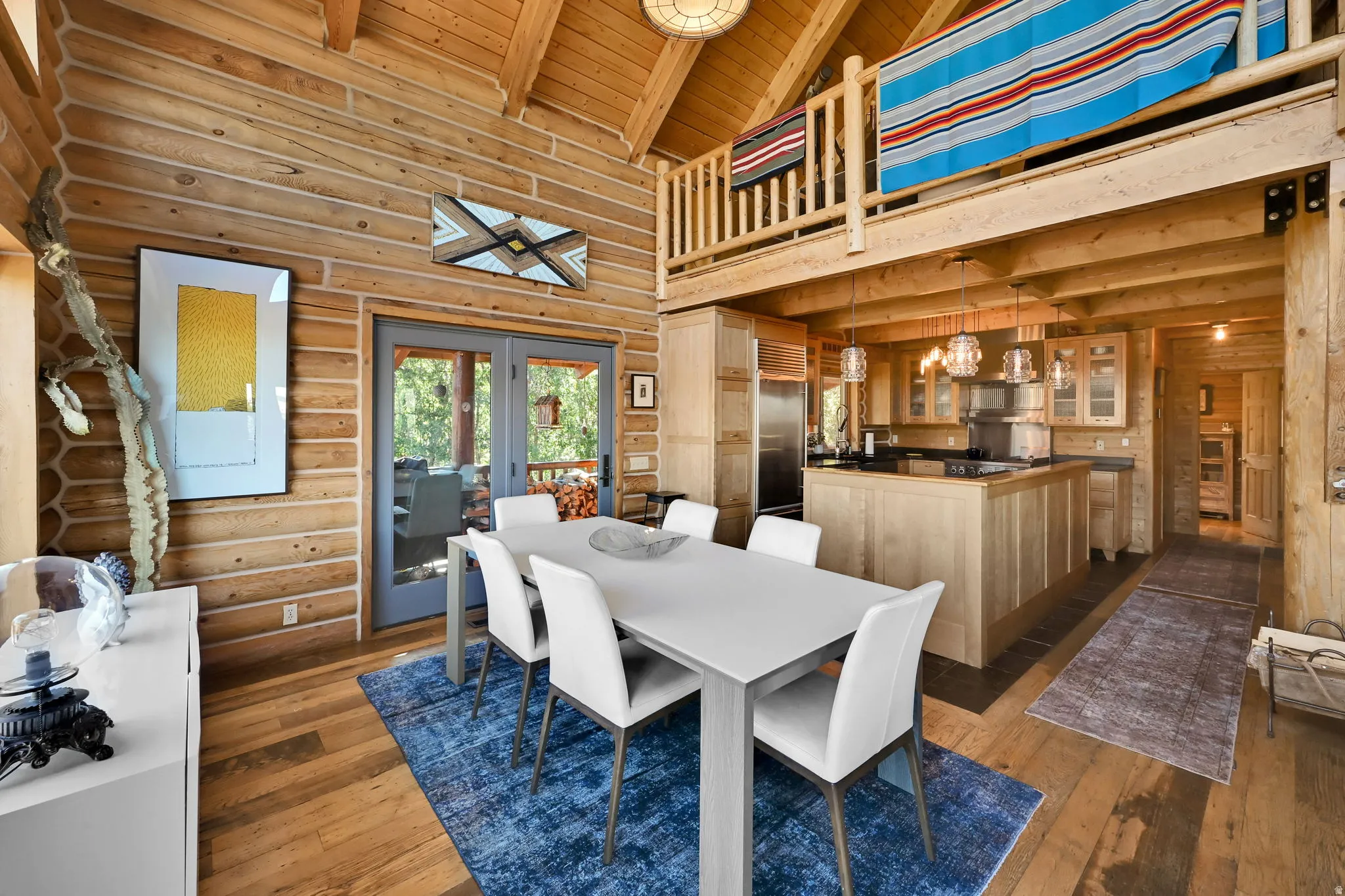 Exposed wood log walls, vaulted wood plank ceilings, wood-finish flooring, and a kitchen featuring a black countertop and pendant lighting