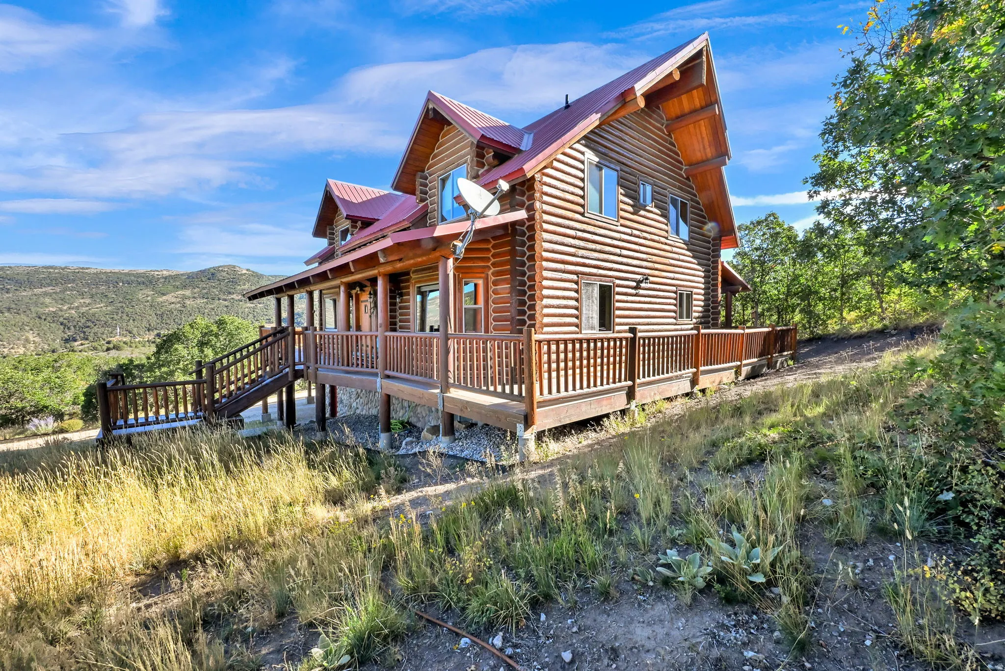 Log cabin exterior featuring multiple windows, a red metal roof, and an expansive wrap-around wood deck with railings